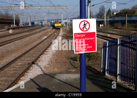 Segnaletica di pericolo sulla stazione ferroviaria piattaforma con treno in avvicinamento Foto Stock