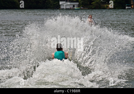 Uomo su uno sci da slalom tirati fuori dall'acqua. Il conducente della barca è appena visibile dietro lo spray. Foto Stock