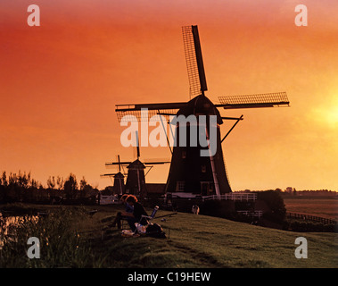 I pescatori sulla riva del canale davanti di mulini a vento al tramonto. Zaanse Schans Mills. Paesi Bassi. Foto Stock