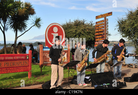 Blue sky vista serale di quattro giovani sassofoni giocando su una pavimentazione erbosa sul lato del Lago Llanquihue, Puerto Varas, Cile Foto Stock