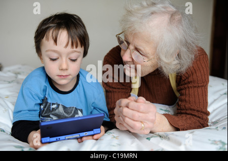 6 anni di giocare sul suo Nintendo DSi e mostrando la sua nonna Foto Stock