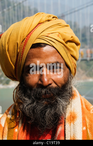 Ritratto di un sadhu con un ponte di sospensione in background, Lakshman Jhula, Fiume Gange, Rishikesh, Uttarakhand, India Foto Stock