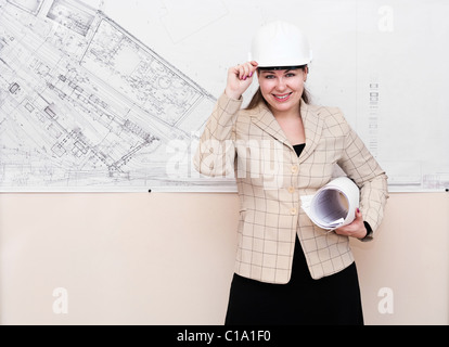 Una giovane donna di un architetto in piedi vicino alla grande blueprint su parete e che mostra Foto Stock