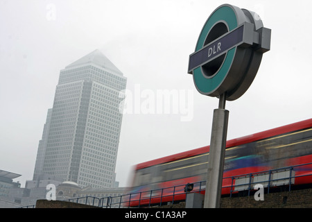 Un segno di DLR con un treno di DLR passando Canary Wharf in background Foto Stock