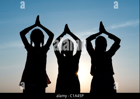 Tre ragazza indiana pregando al tramonto. India. Silhouette Foto Stock