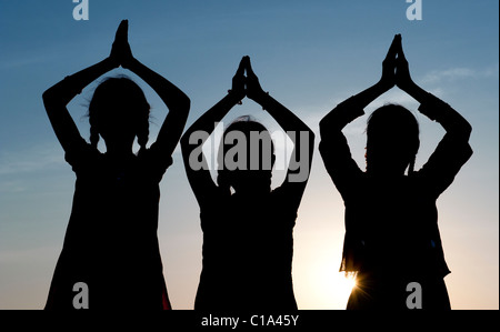 Tre ragazze indiano pregando al tramonto. India. Silhouette Foto Stock