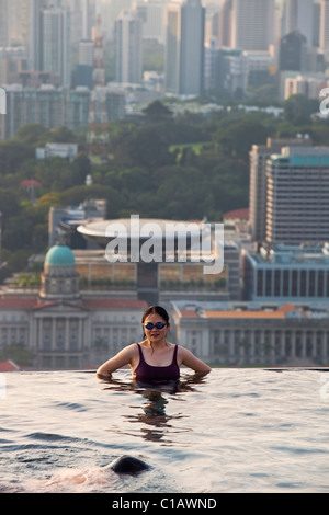 Donna di nuoto in piscina presso il Marina Bay Sands SkyPark con lo skyline della città in background. Il Marina Bay, Singapore Foto Stock