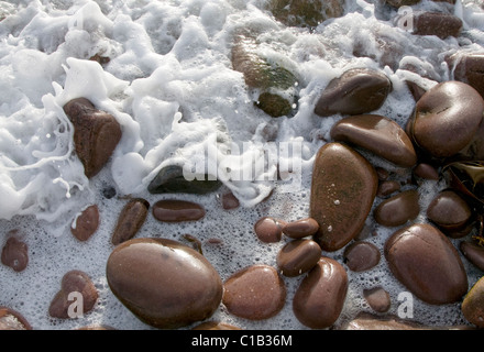 Dettaglio dell'acqua di mare spume o schiuma bianca il lavaggio più lisci ciottoli rosso sulla spiaggia di Applecross, Highlands scozzesi Foto Stock