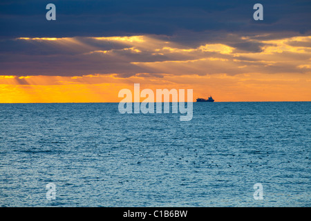 Tramonto attraverso le nuvole nel mare con la nave da carico off Brighton Foto Stock