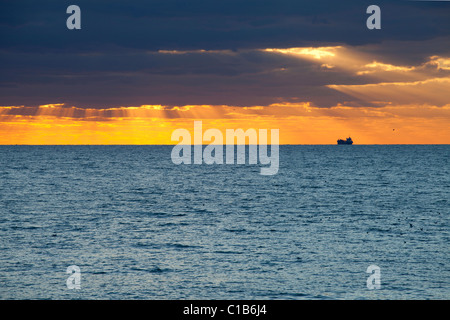 Tramonto attraverso le nuvole nel mare con la nave da carico off Brighton Foto Stock