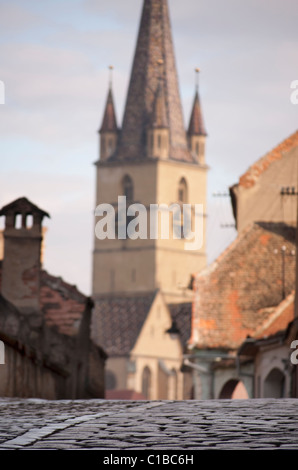Campanile di una chiesa in Sibiu Romania fuori fuoco, concentrandosi sui ciottoli pavimentazione di pietra street Foto Stock