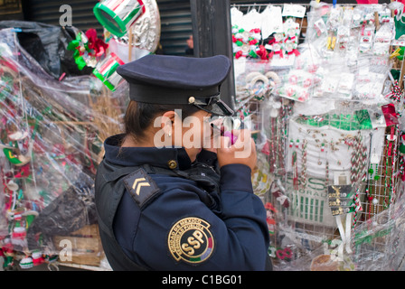 A Città del Messico poliziotta si applica il suo trucco nella parte anteriore di una via di stand di vendita patriottico commemorativo degli articoli. Foto Stock