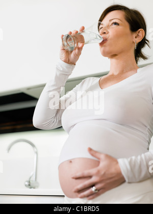 Ritratto di italiano di 6 mesi donna incinta acqua potabile in cucina. Forma verticale, spazio di copia Foto Stock