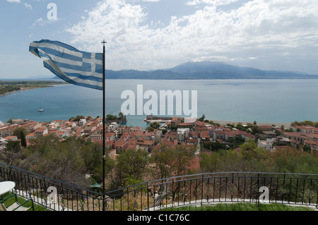 Una bandiera greca oscilla nel vento in alto sopra la città di Nafpaktos e il golfo di Corinto. Foto Stock