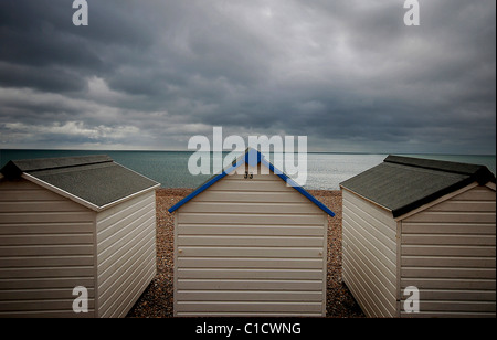 Moody vista con cielo scuro, design simmetrico con tre cabine sulla spiaggia, guardando sopra un mare calmo di essere sopraffatte da un cielo tempestoso. Foto Stock