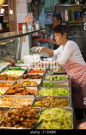 Donna che serve da molti piatti in un Hawker stallo a persone del Parco del complesso. Chinatown, Singapore Foto Stock