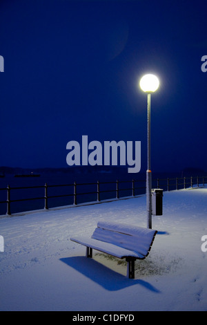 Una panchina nel parco coperto di neve a notte Foto Stock