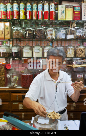 Un bottegaio pesa gli ingredienti in una medicina tradizionale cinese shop. Chinatown, Singapore Foto Stock