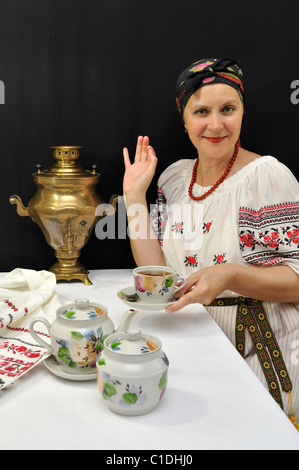 Signora in tradizionali abiti ucraino che offre una tazza di tè da samovar su nero Foto Stock