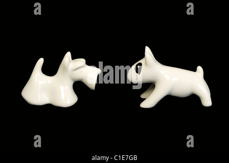 Due ceramiche bianche cani bull terrier con punto bianco e scottish terrier di fronte e isolato su nero Foto Stock