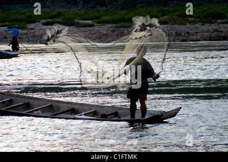 Un pescatore in una barca di legno è di gettare una rete da pesca sul fiume Mekong a Luang Prabang, Laos. Foto Stock