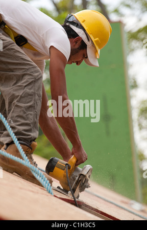 Falegname ispanica utilizzando una sega circolare sul pannello del tetto di una casa in costruzione Foto Stock