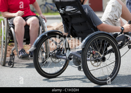 Ragazzo con tendinite in bici e una donna con malattie degenerative anca in una sedia a rotelle Foto Stock