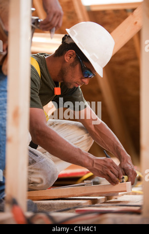 Falegname ispanica segnando una misurazione su un bordo in corrispondenza di una casa in costruzione Foto Stock