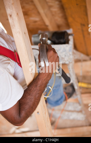 Falegname ispanica utilizzando un martello in una casa in costruzione Foto Stock
