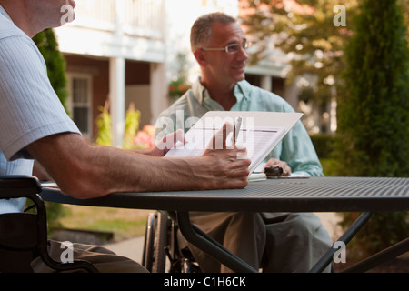 Uomo con Friedreich tenendo una penna con mani degenerata seduto con un uomo con lesioni del midollo spinale Foto Stock