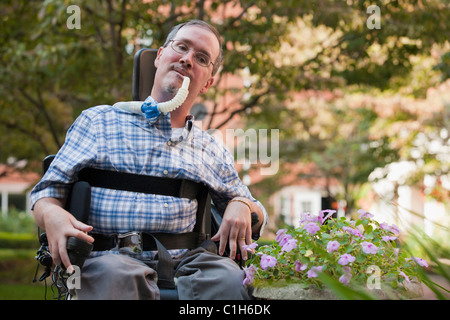 L'uomo con la distrofia muscolare di Duchenne seduto in una sedia a rotelle con un ventilatore di respirazione Foto Stock