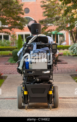 Vista posteriore di un uomo con la distrofia muscolare di Duchenne in una sedia a rotelle motorizzata su strada Foto Stock