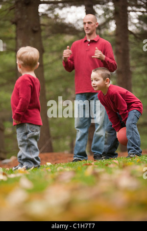 L'uomo firma la parola 'Play' in American Sign Language mentre gioca con i suoi figli in un parco Foto Stock