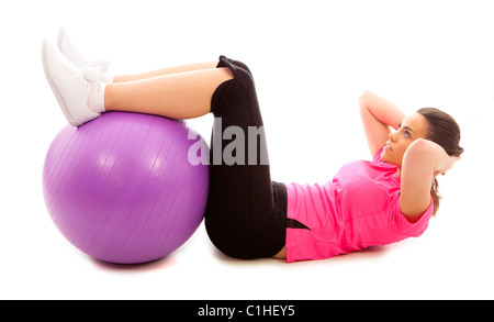 Una giovane donna facendo un crunch addominale utilizzando un viola palla ginnica Foto Stock