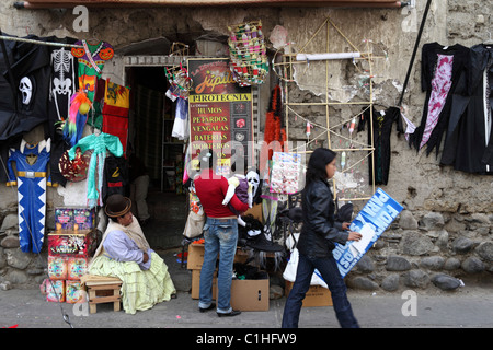 Donna Aymara seduta fuori dall'ingresso del negozio che vende fuochi d'artificio maschere e costumi per Halloween, la Paz, Bolivia Foto Stock