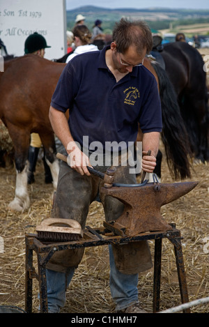 Fabbro maniscalco rendendo pattini del cavallo su un incudine in Cornovaglia del cavallo e del paese mostrano Foto Stock