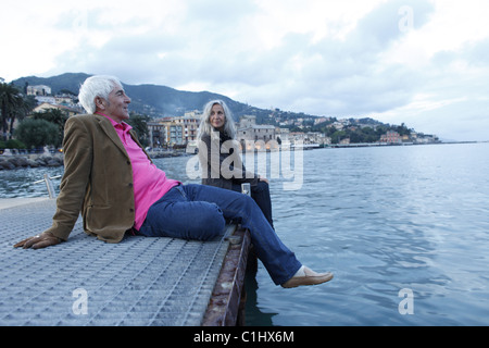 Coppia senior seduto su di un molo dall'acqua, Italia Foto Stock