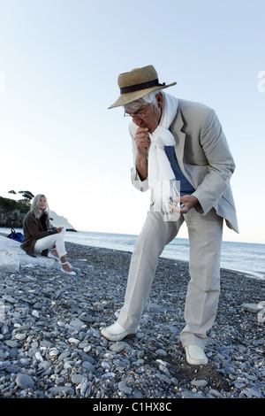 Senior uomo guardando pietre sulla spiaggia, Italia Foto Stock