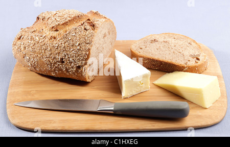 Piatto in legno di fresco con granaio scolpito in legno di noce con pane e formaggio due cunei collocati su un blu pallido tovaglia. Foto Stock