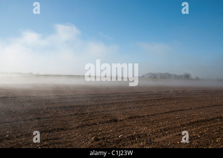 La nebbia che salgono dal campo la mattina presto luminoso caldo sole brucia fuori l'acqua dal campo arato Foto Stock