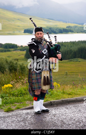 Un Piper sopra Loch Tulla nelle Highlands scozzesi Foto Stock