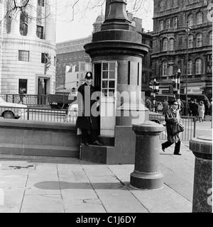 1960s, un agente di polizia britannico in piedi alla cabina di polizia di Trafalgar Square, Westminster, Londra, la più piccola stazione di polizia britannica. Foto Stock
