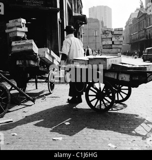 Anni '1950, facchino al famoso mercato del pesce di Billingsgate che tira un carro di legno carico di casse di pesce congelato a Lower Thames St, Londra, Inghilterra. Foto Stock