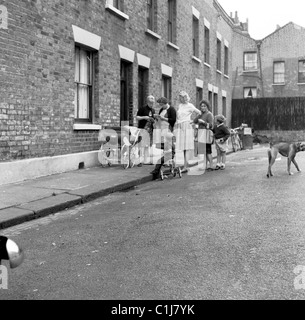 Anni Cinquanta a Londra, Inghilterra, storico, Vittoriano case a schiera, piccolo gruppo di madri al di fuori in strada con i loro figli, pram e triciclo. Foto Stock