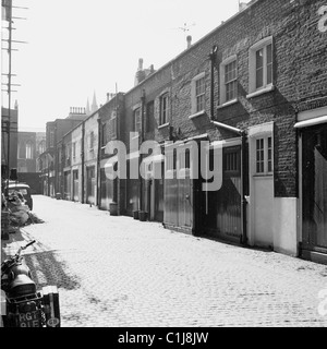 Anni '1950, storica, una strada acciottolata di case mews a Kensington, West London, con garage al livello della strada e alloggi sopra. Foto Stock