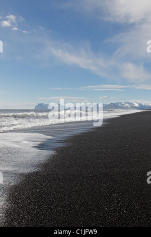 Onde sbarcano su un nero spiaggia vulcanica in Islanda con le montagne sullo sfondo Foto Stock