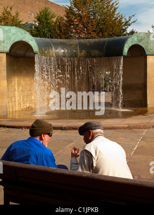 Due uomini su una panchina a parlare davanti alla fontana nella piazza del mercato in Derby city centre Derbyshire England Regno Unito Foto Stock