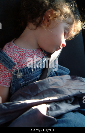 Bambina addormentata nel retro di un auto con una cintura di sicurezza su Foto Stock