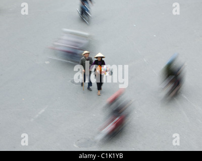 Un vecchio uomo e donna navigare il loro modo attraverso la moto su una strada trafficata nel cuore di Hanoi, Vietnam Foto Stock