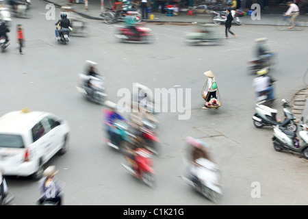Un giogo carrier donna passi nel traffico in Hanoi, Vietnam Foto Stock